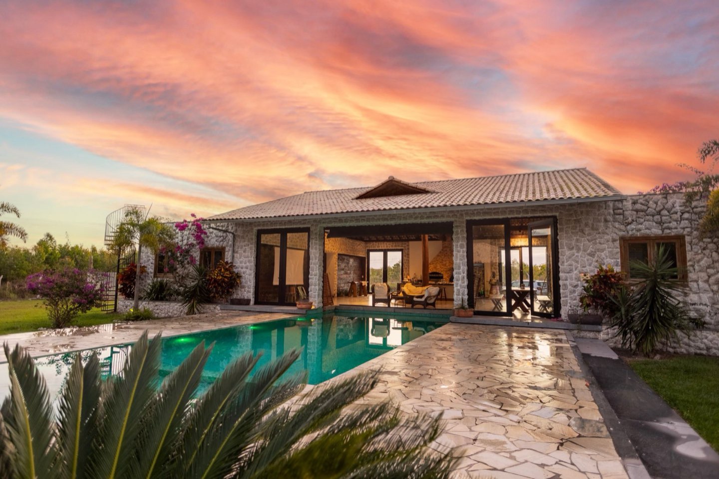 A backyard in-ground pool and patio glowing at dusk.