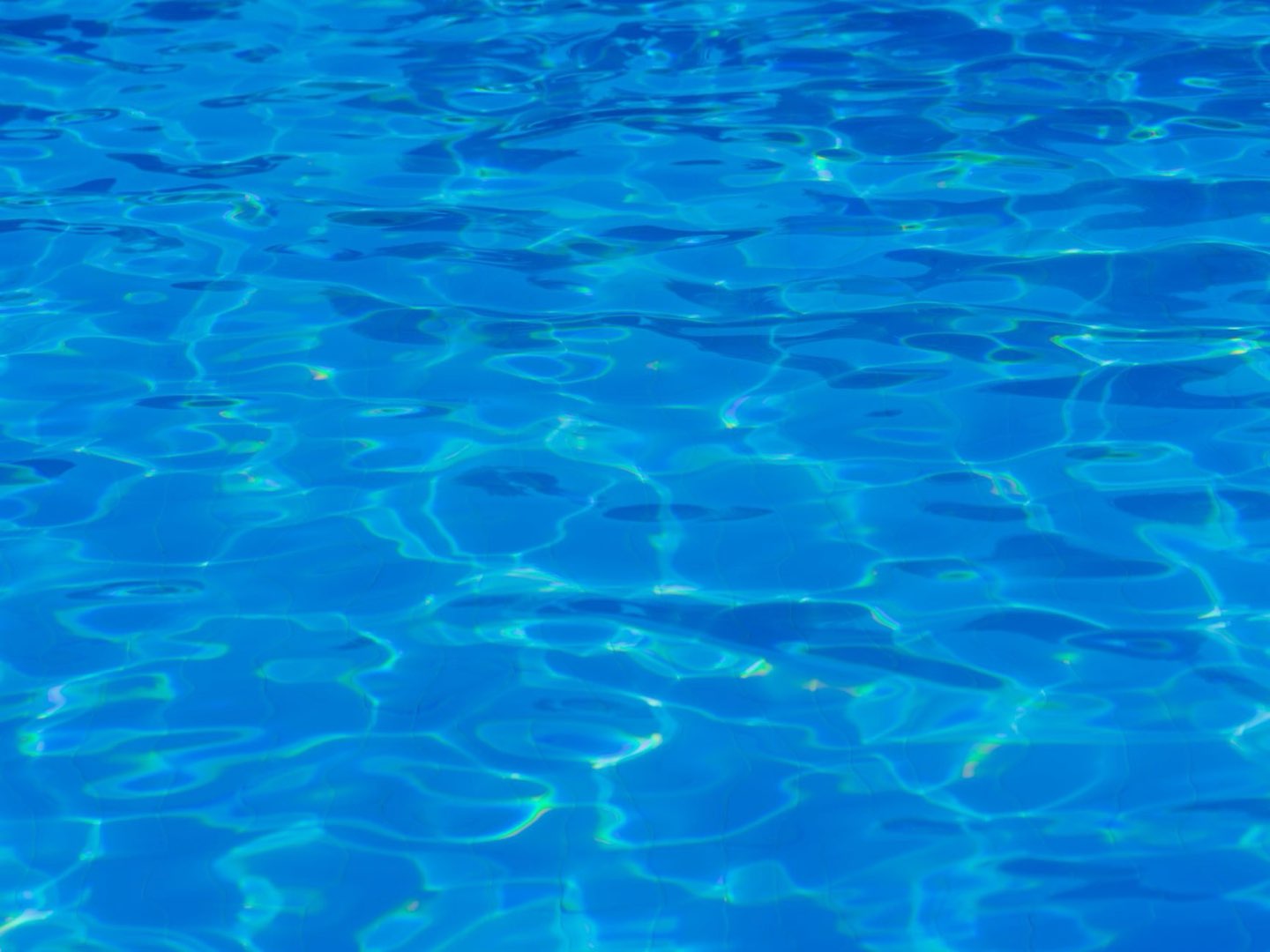 Sunlight on the clear blue surface of a swimming pool.
